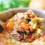 Closeup of ladle of soup over pot.