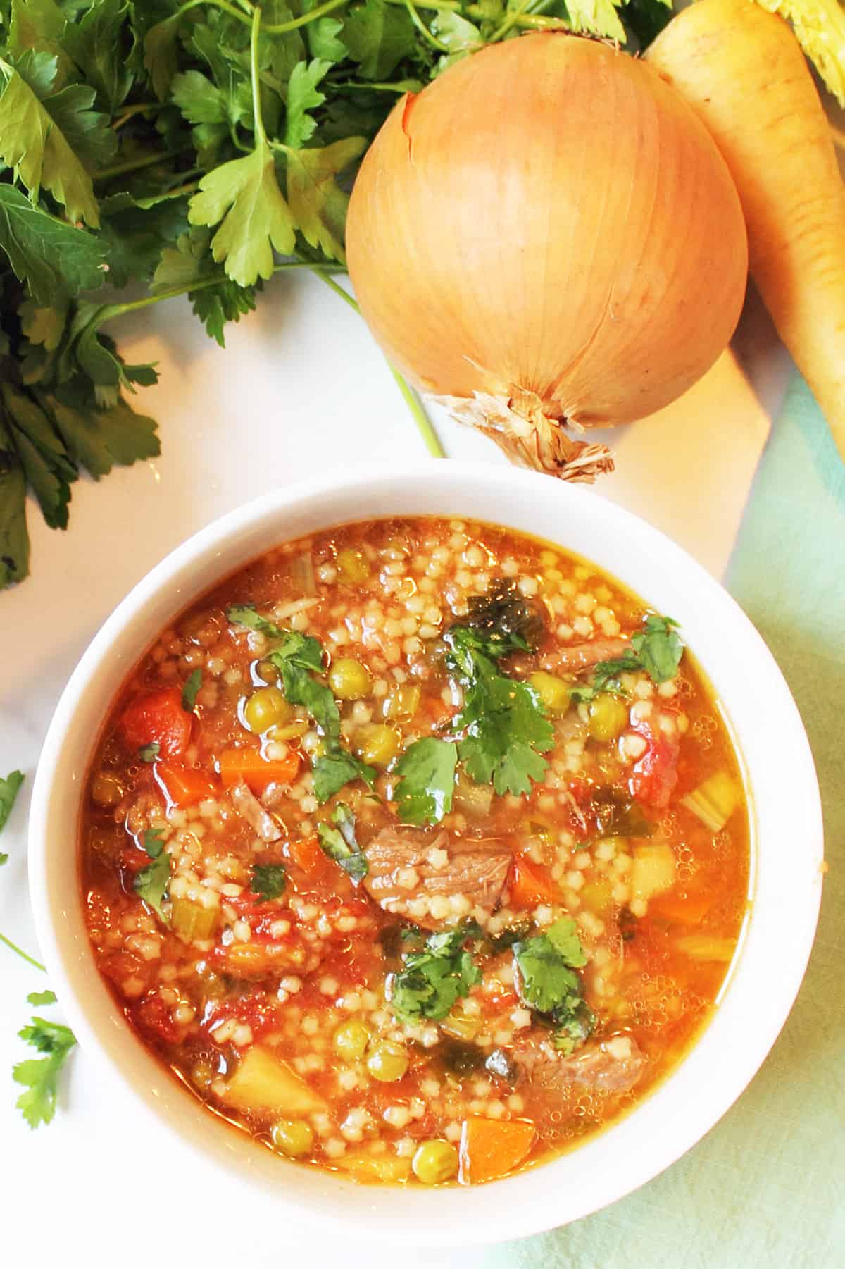 Bowl of vegetable beef soup next to whole vegetables.
