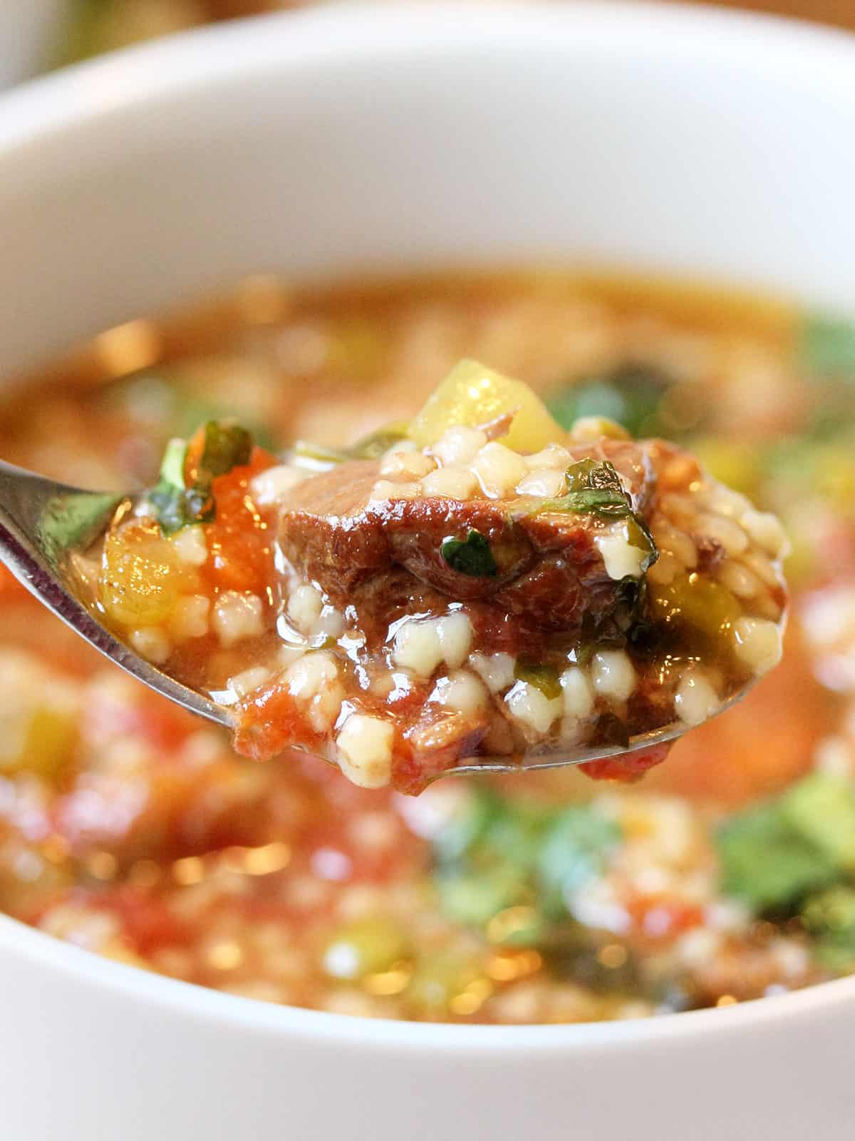 Spoonful of homemade vegetable beef soup closeup over bowl.
