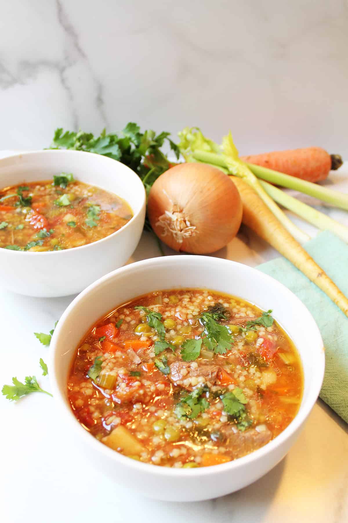 Tow bowls of vegetable beef soup on white marble table.