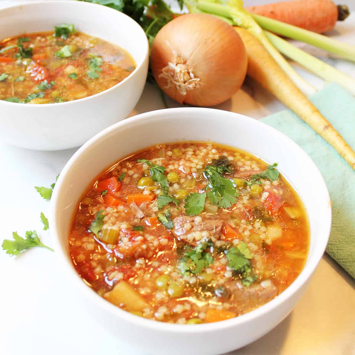 Two bowls of soup with fresh vegetables.
