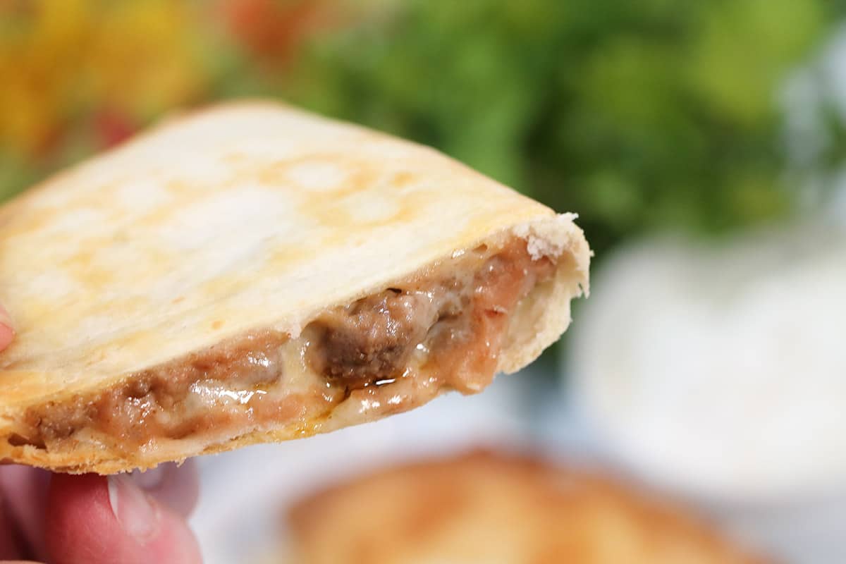 Holding cheesy beef quesadillas showing filling.