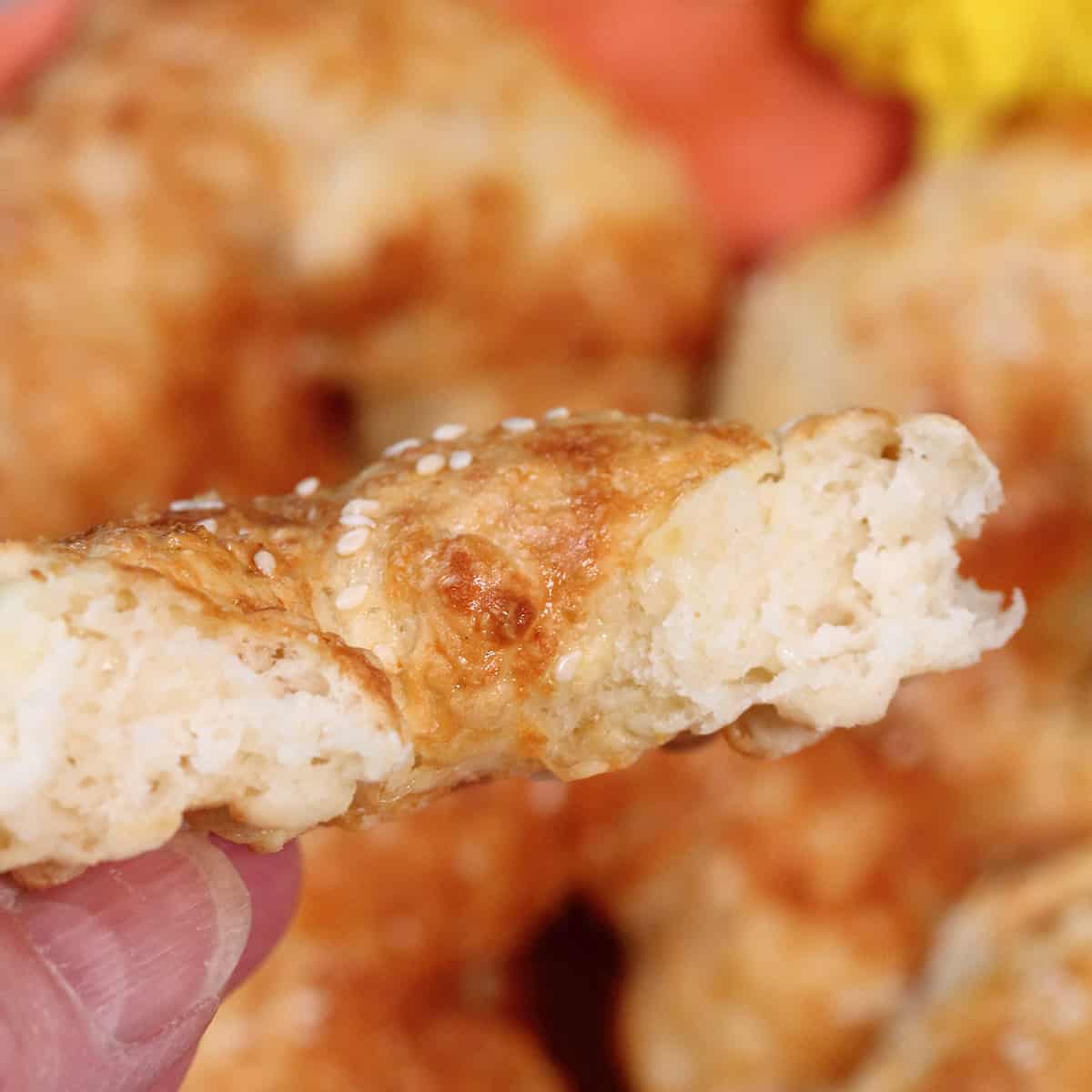 Holding half a cheese bagel over basket.