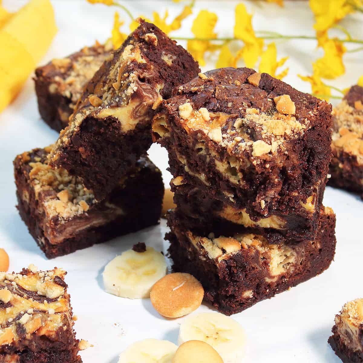 Stack of brownies on white table with yellow flowers.