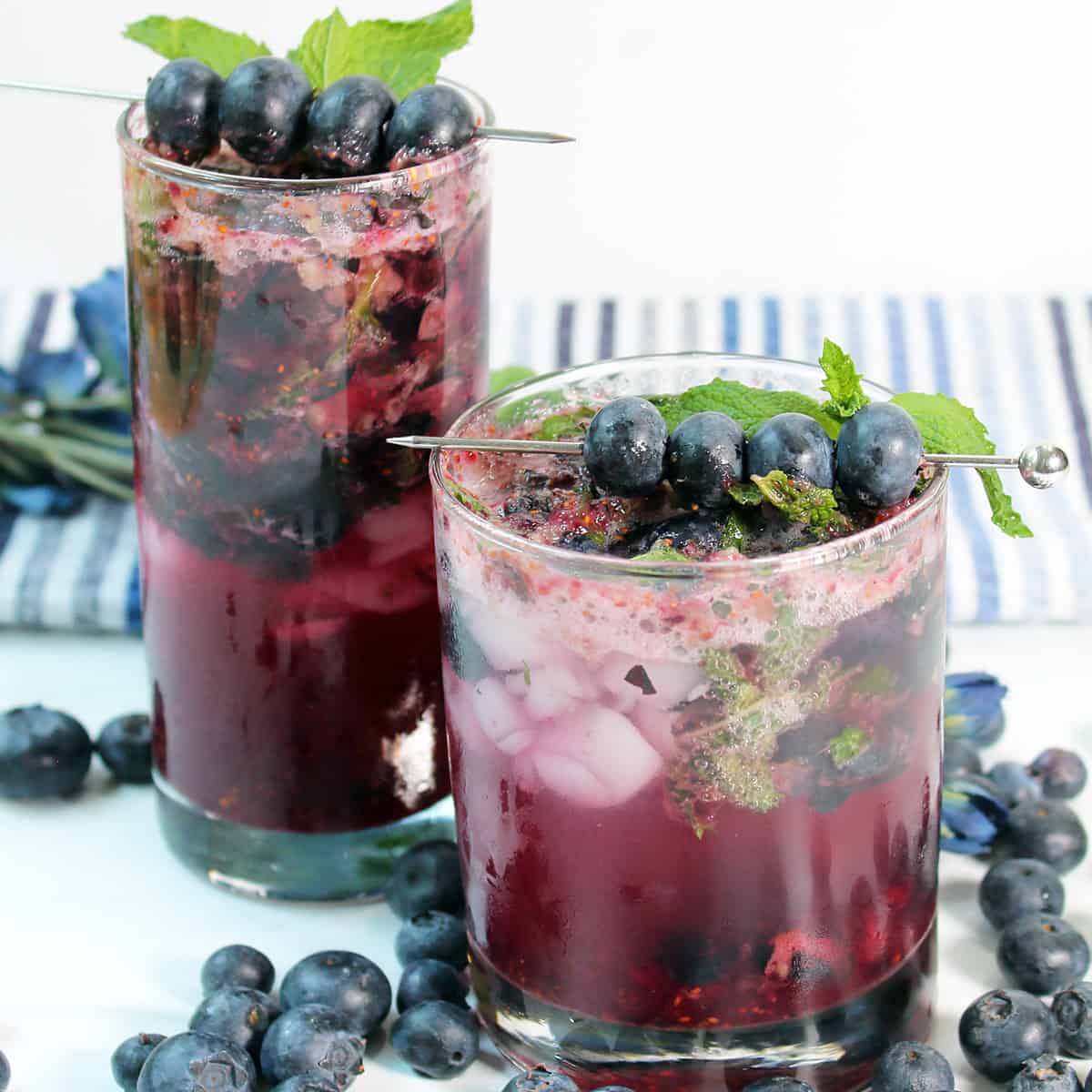 Two blueberry mojitos with blueberries on white table.