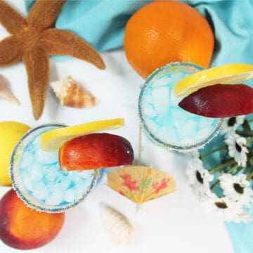 Overhead of blue mermaid drink with peach and lemon garnish.