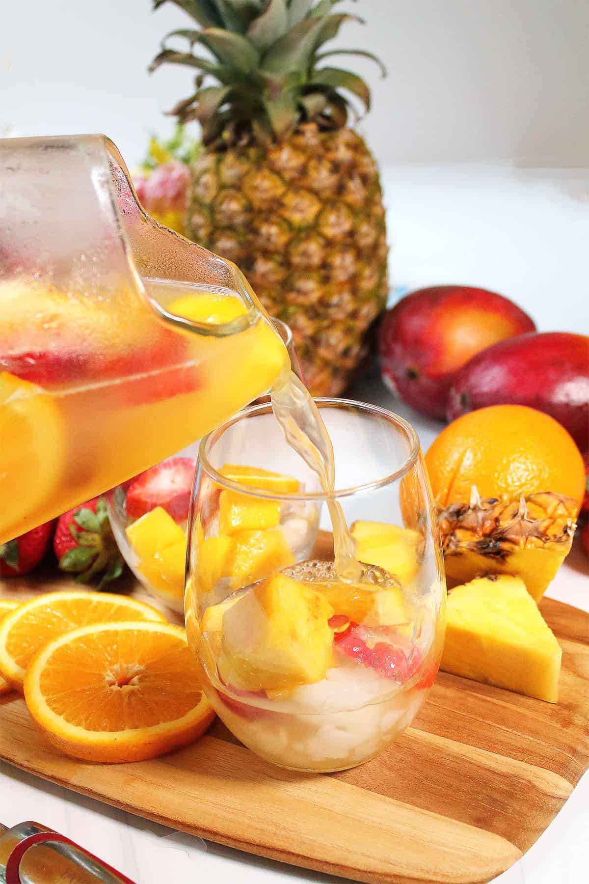 Pouring sangria over fruit in glasses.