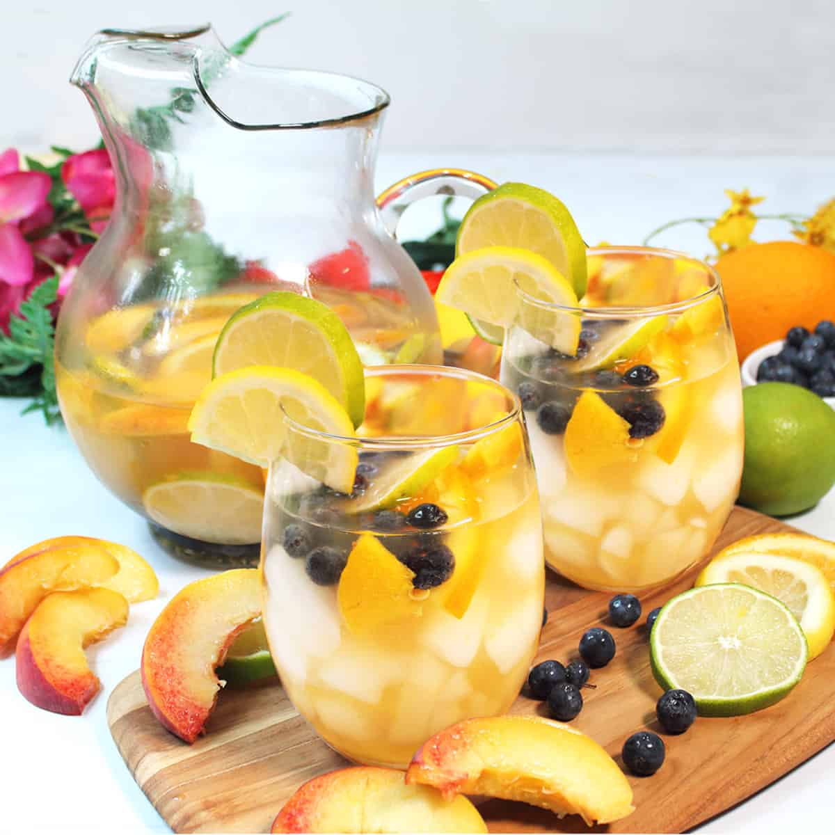 Glasses filled with fruit and sangria on wooden board.