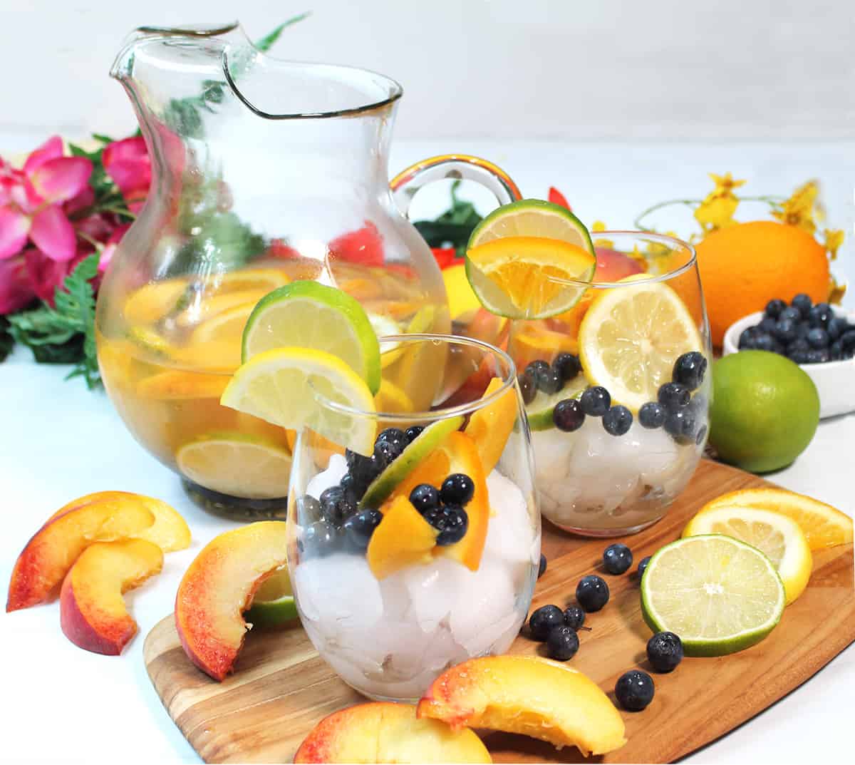 Glasses filled with fruit with full pitcher of peach schnapps sangria in back.