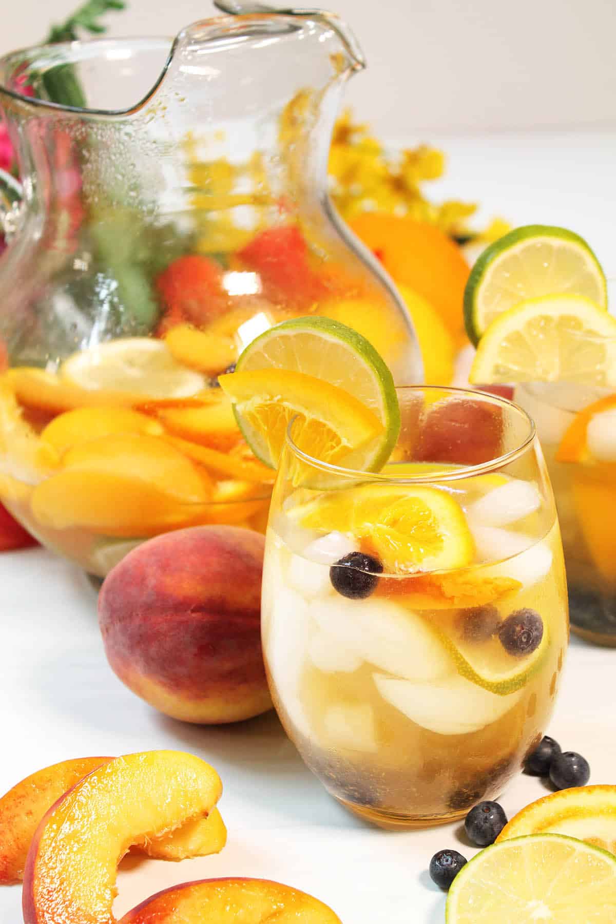 Single glass of peach sangria with pitcher in back.