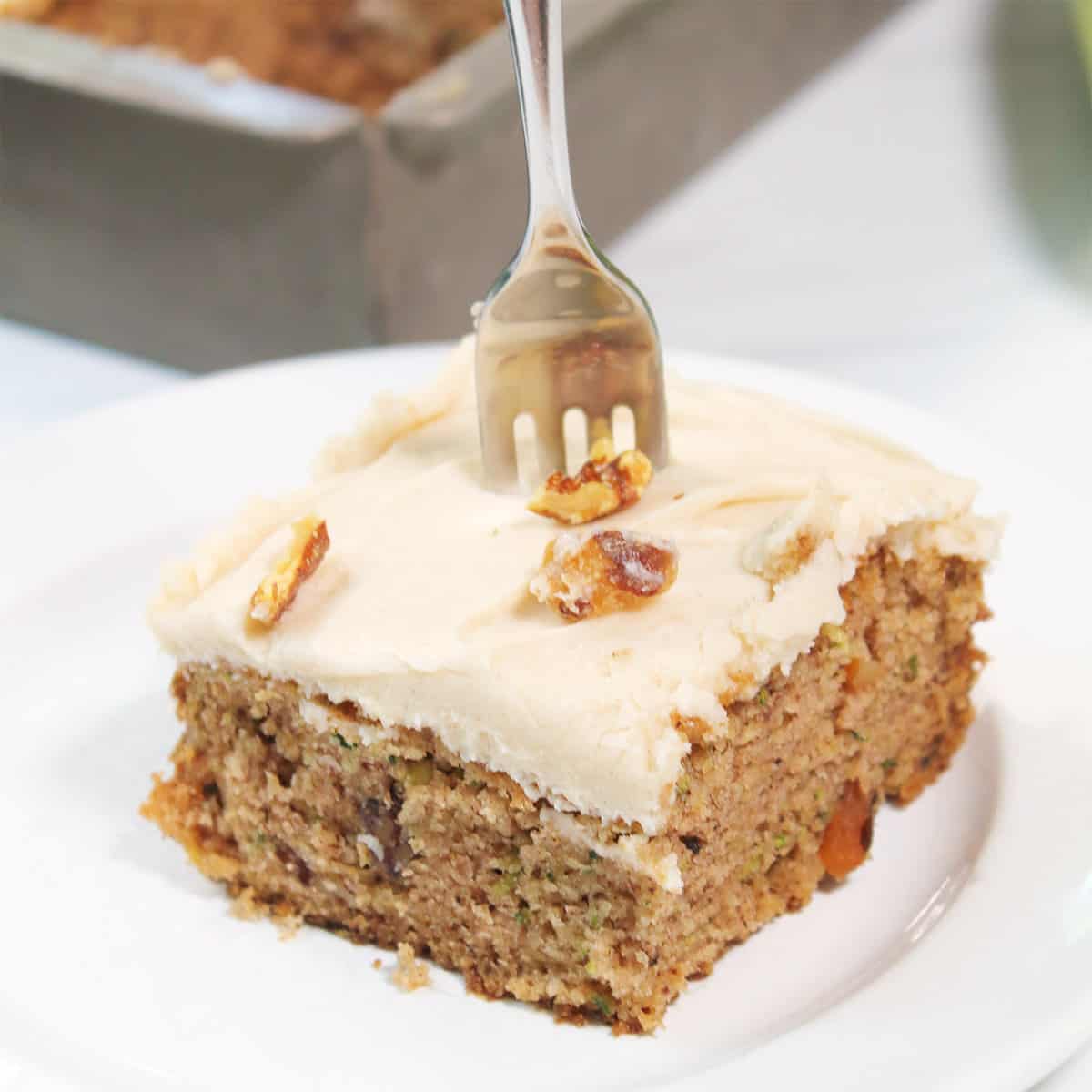 Slice of zucchini cake with cream cheese frosting with fork in it.