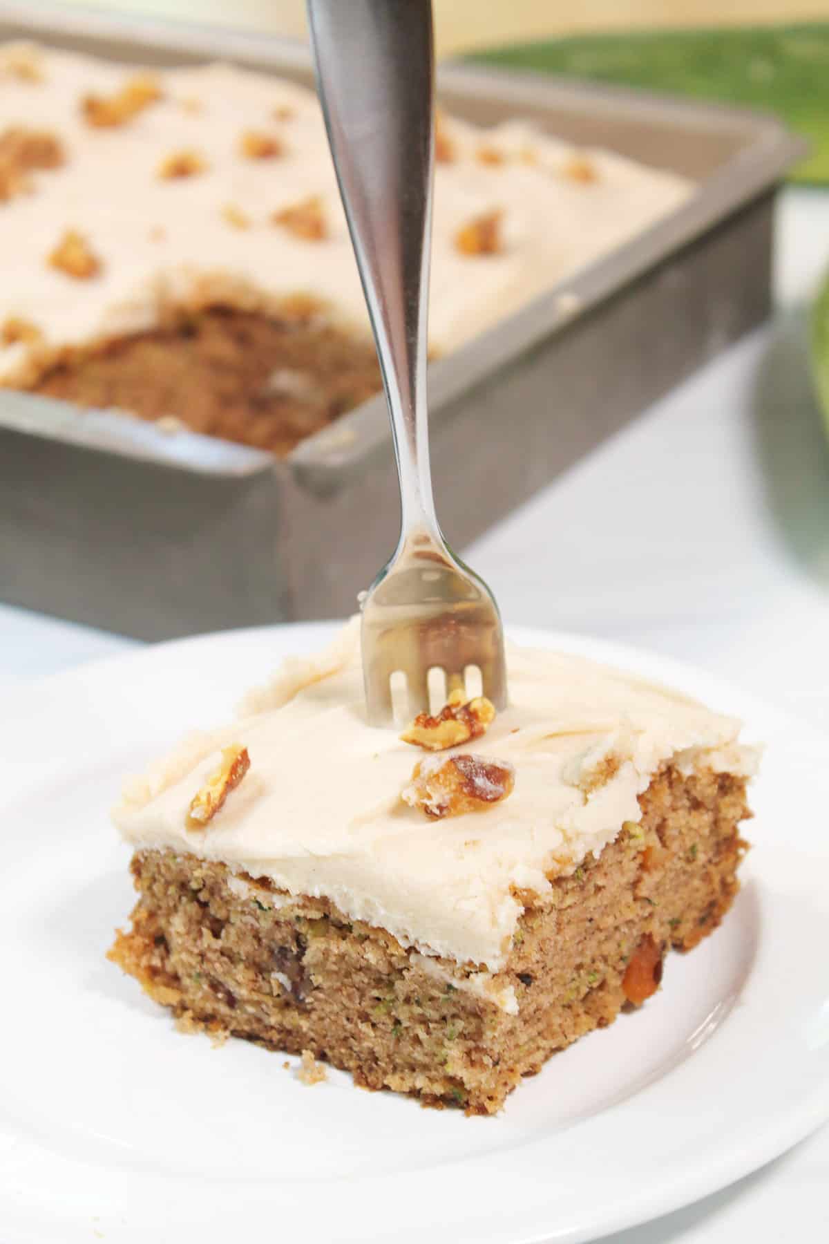 Slice of zucchini cake with cream cheese frosting with fork in it.