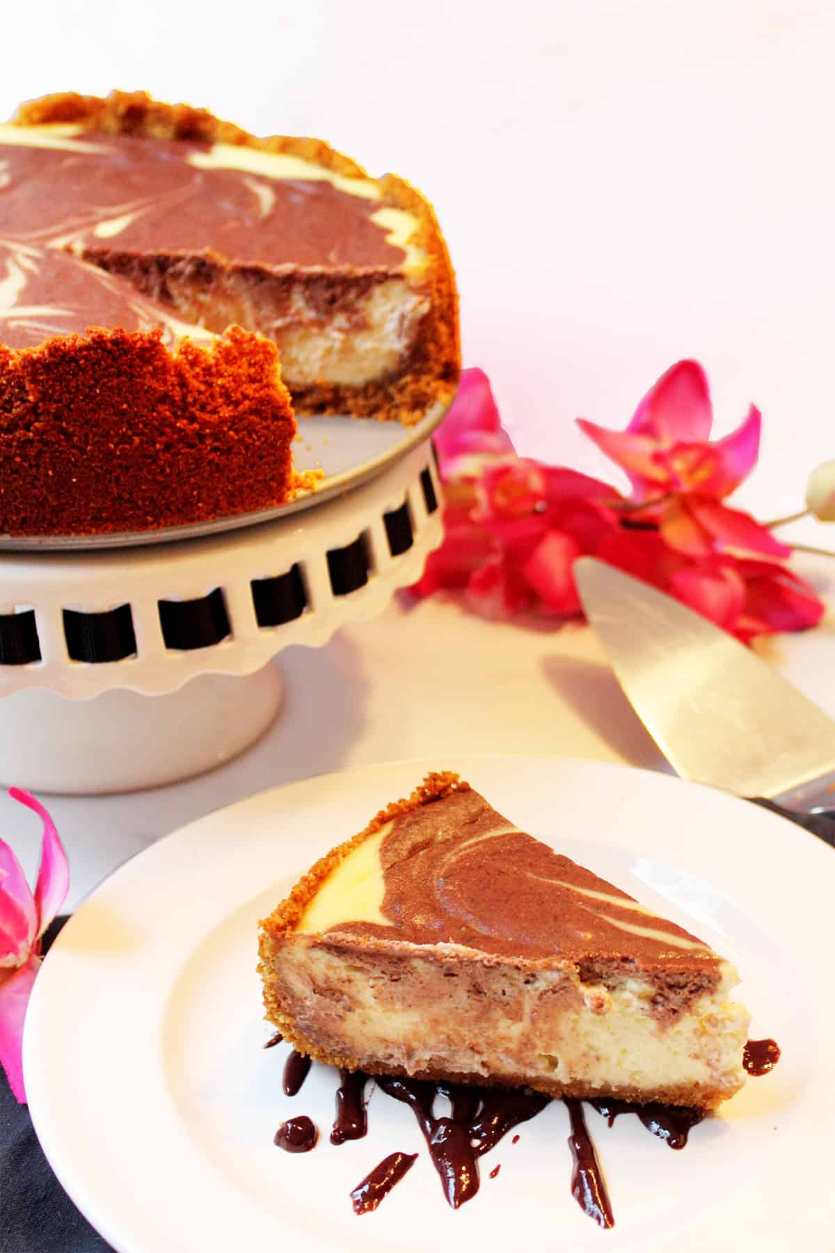 Full chocolate and vanilla cheesecake on cake stand with slice in front.