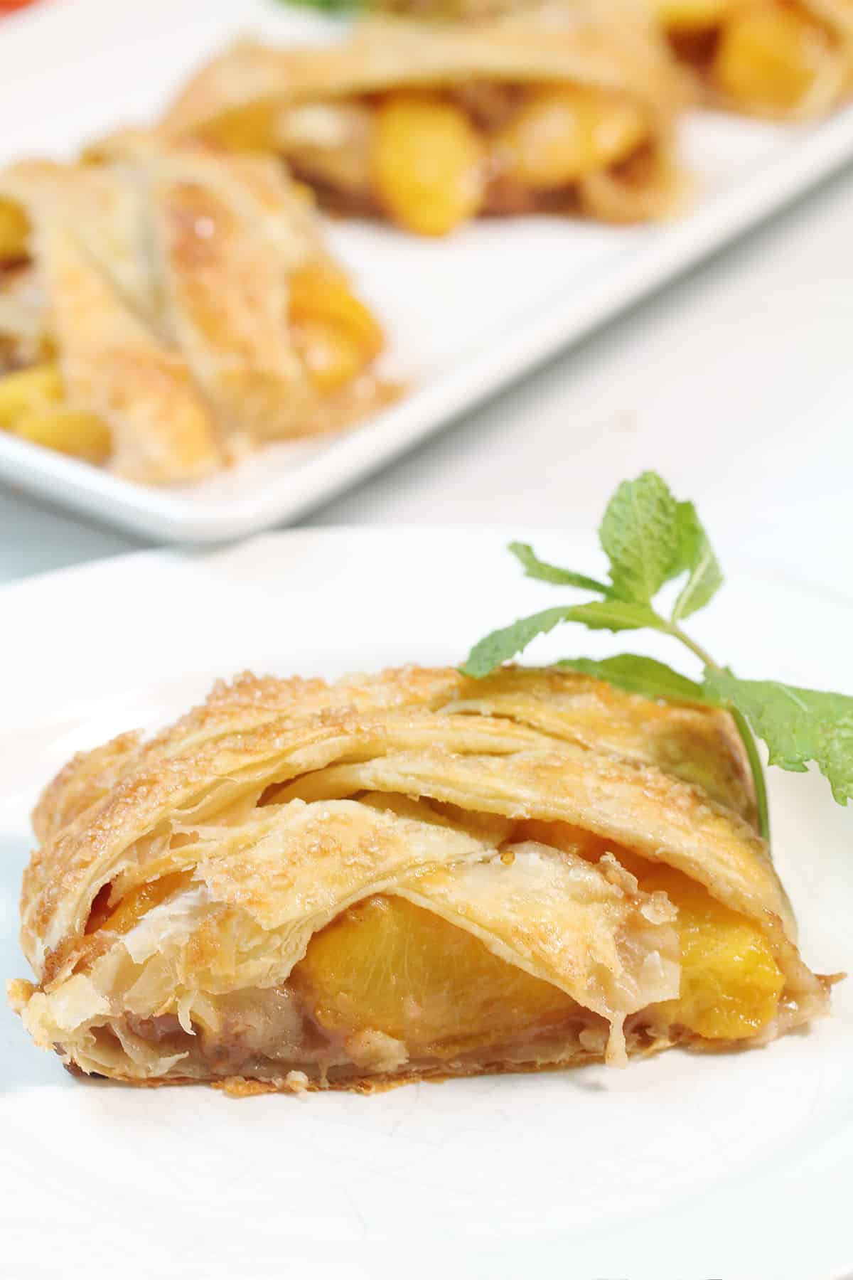 Slice of Peach Studel on plate with full strudel in back.