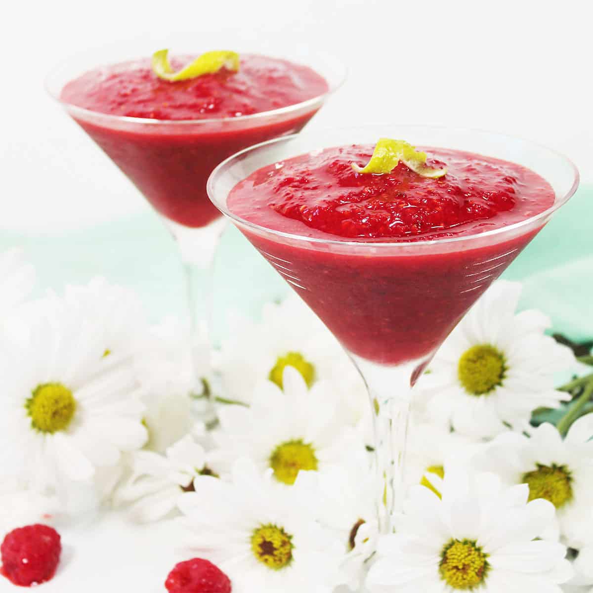 Two rapberry daiquiri drinks among daisies.