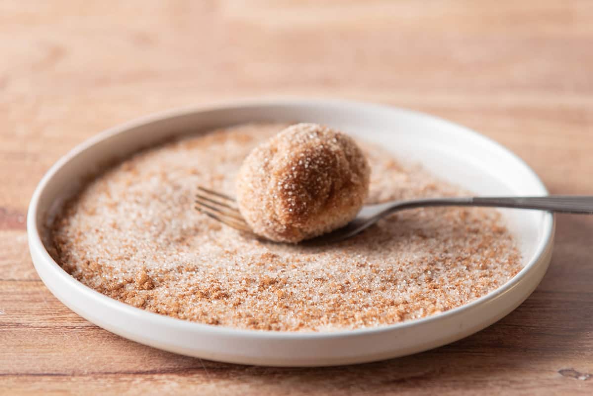 Rolling donut hole in cinnamon sugar.
