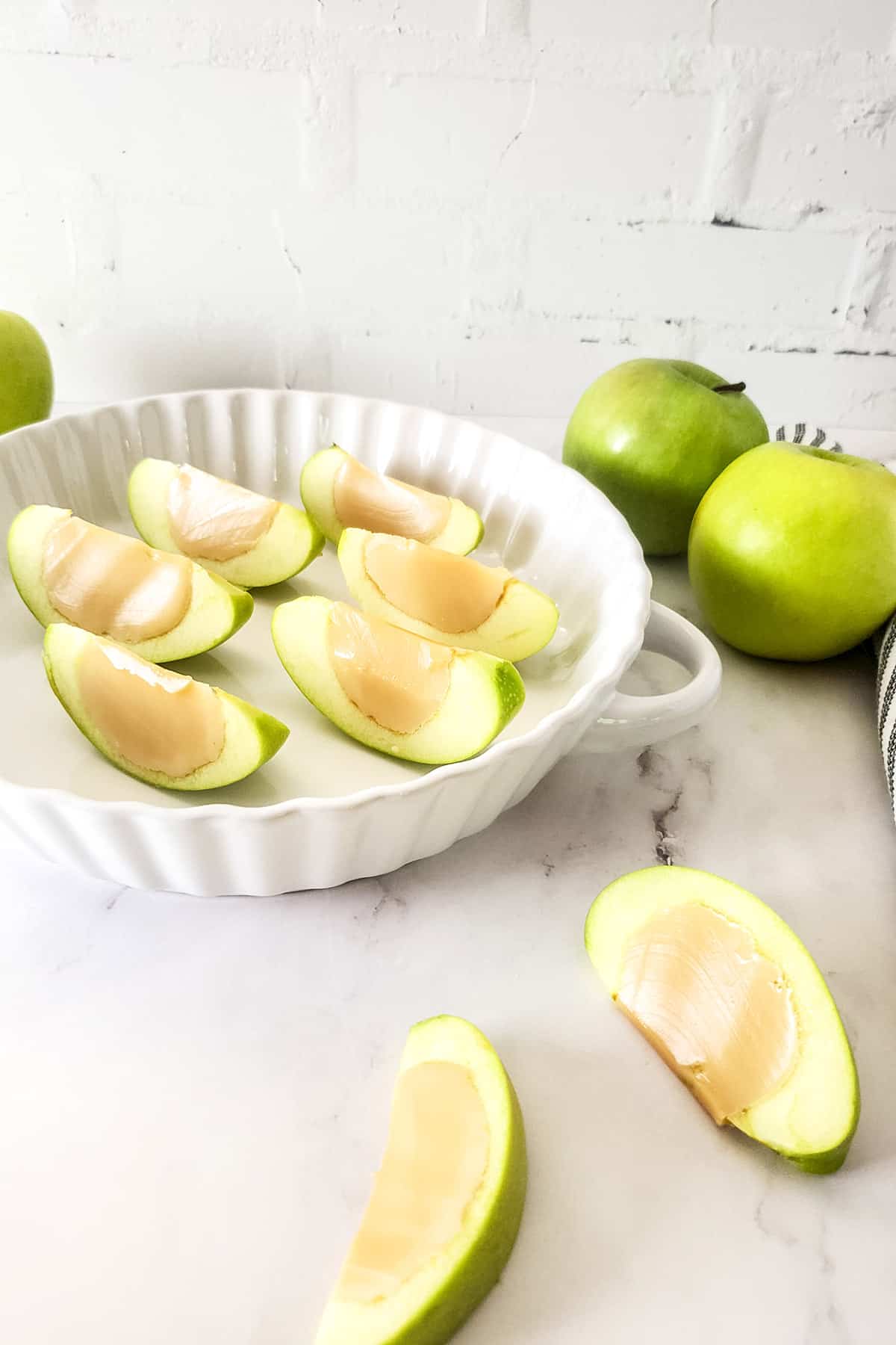 Filled dish with apple shots with two on table.