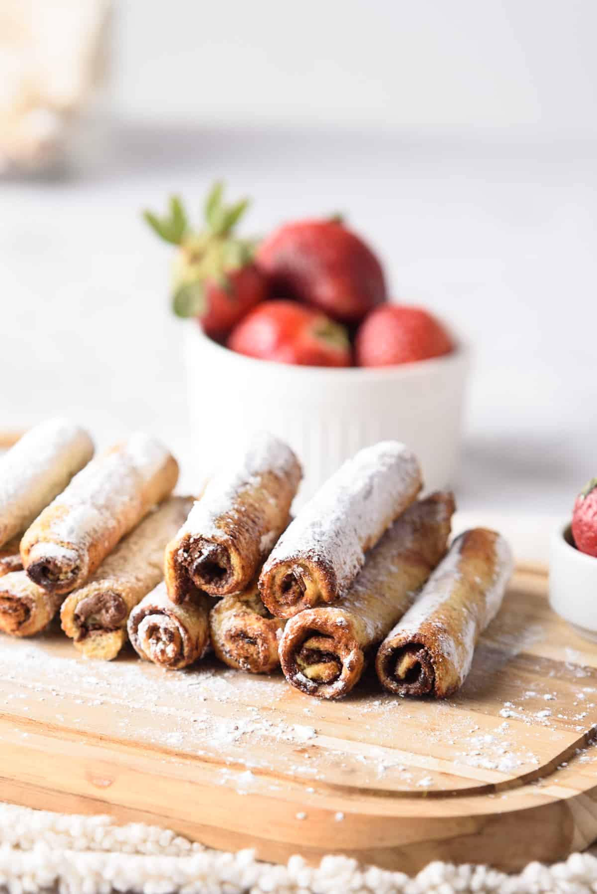 French Toast Rollups on wooden board with strawberries in back.