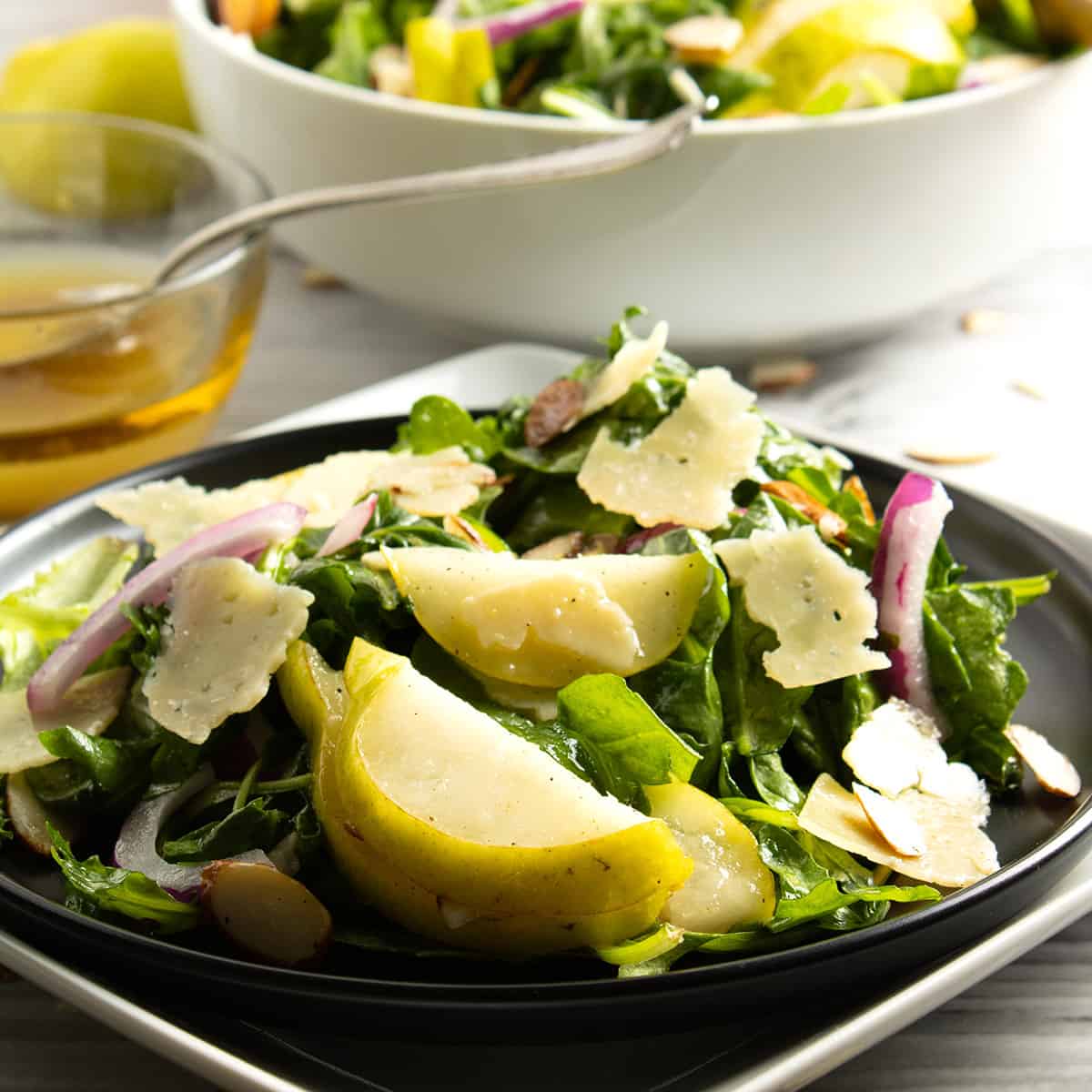 Arugula Salad with pear on plate with bowl in background.