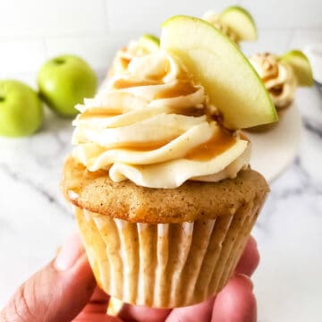 Holding cupcake with frosting and apple garnish.