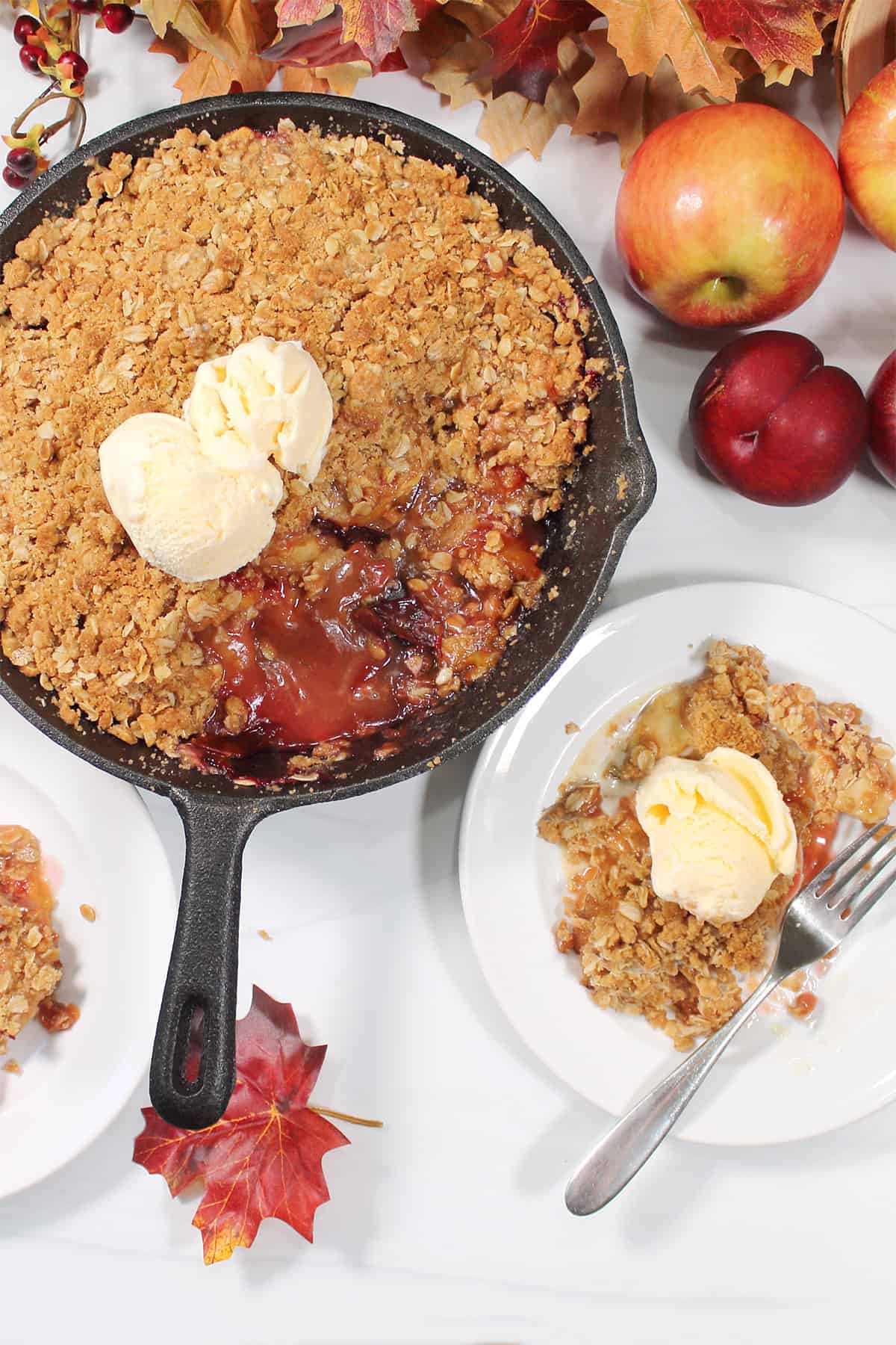 Overhead of apple and plum crumble in skillet with serving on plate with ice cream.
