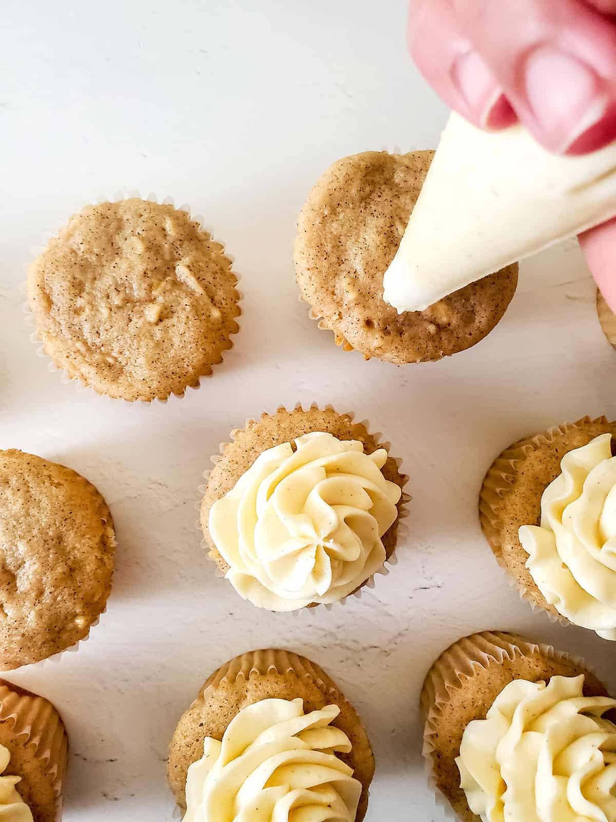 Piping frosting on cupcakes.