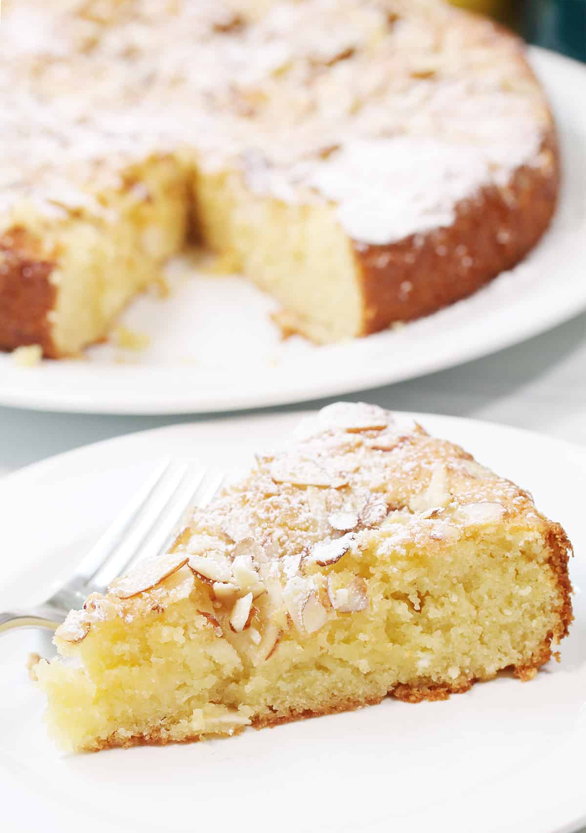 Slice of cake on plate in front of pear almond cake.