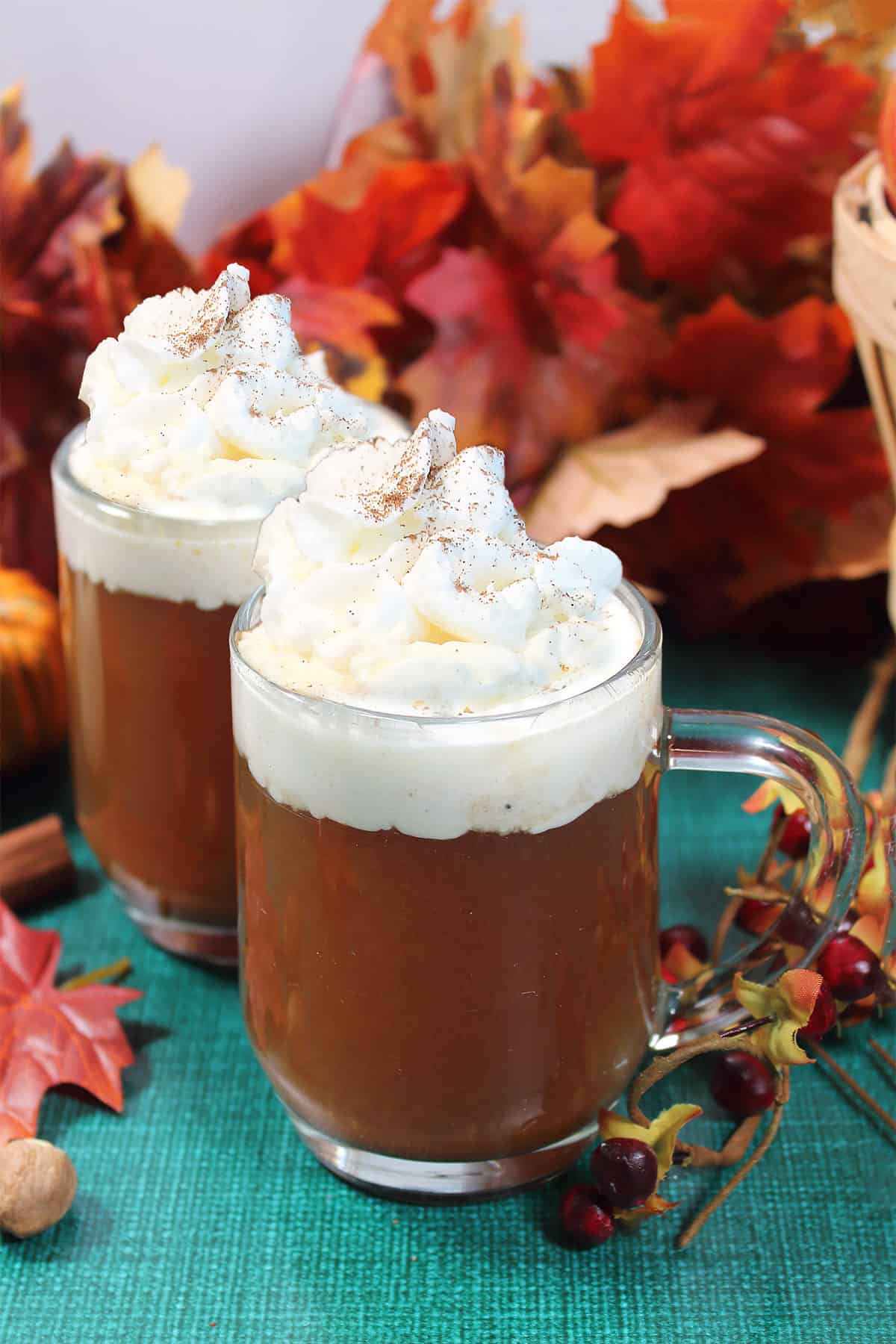 Two mugs of spiked apple cider garnished with whipped cream.