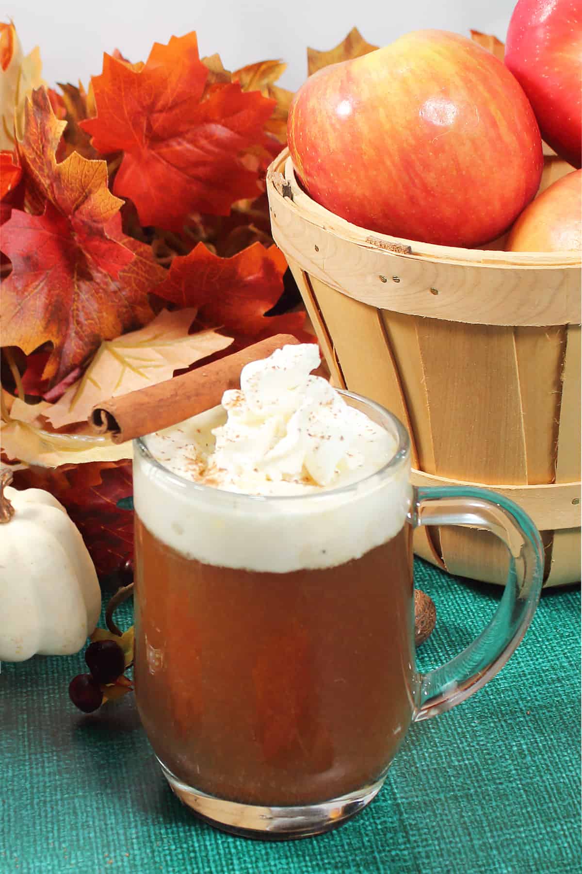 Hot apple cider cocktail in front of basket of apples.