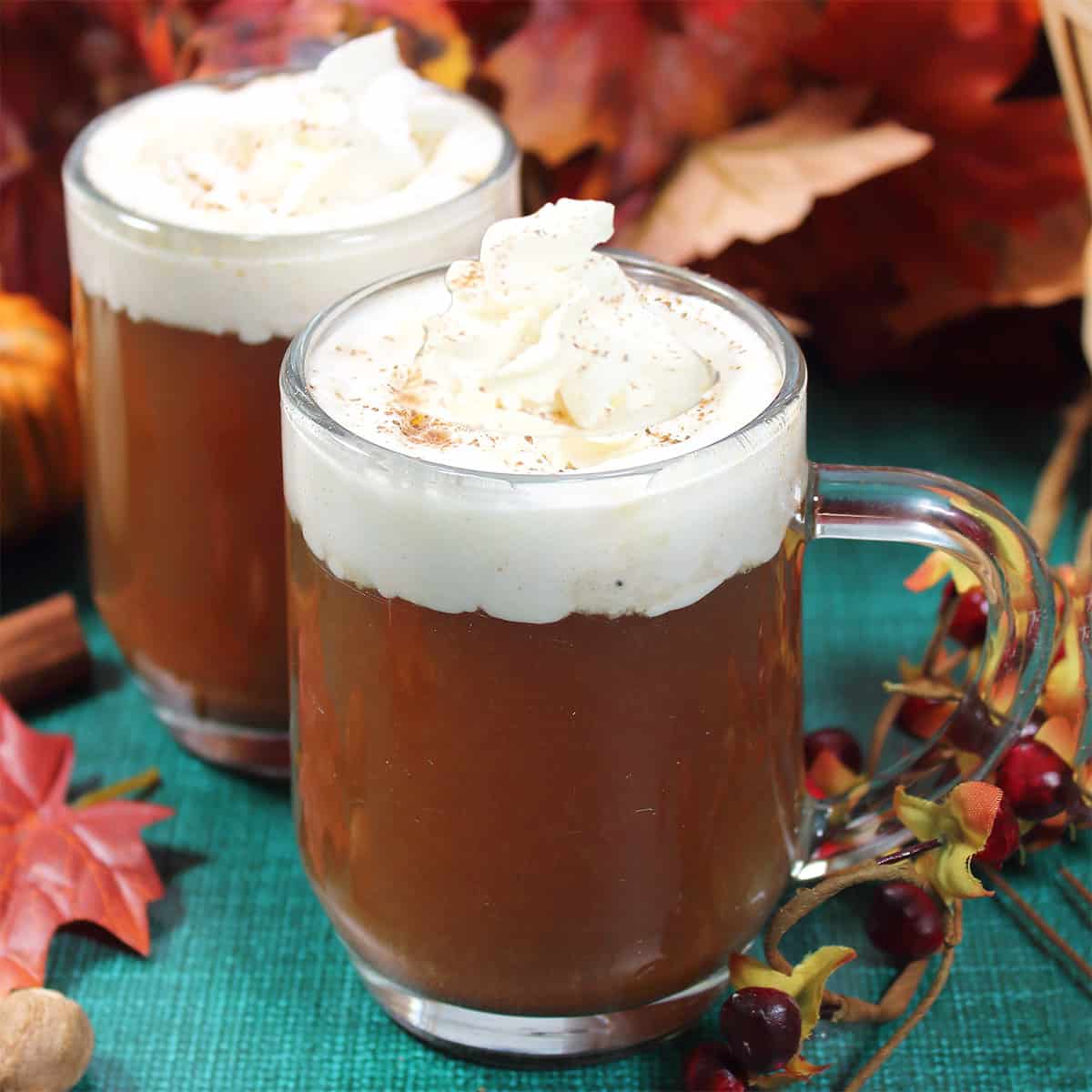 Two mugs of hot spiked apple cider with whipped cream.