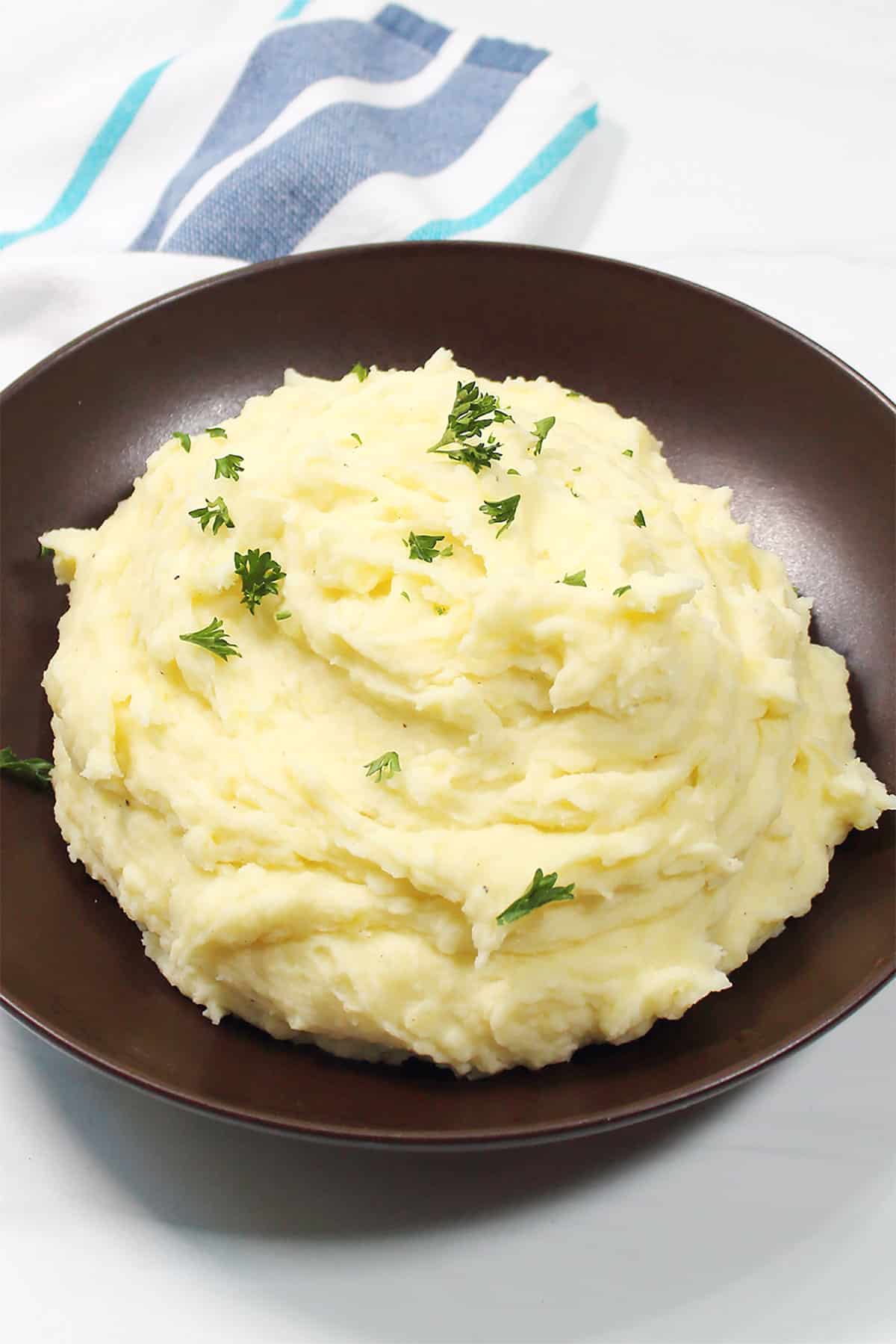 Bowl of creamy mashed potatoes with parsley garnish.