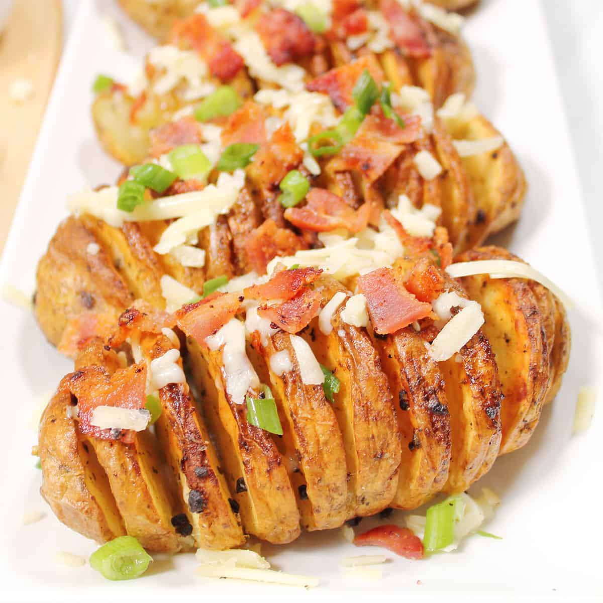 Platter of hasselback potatoes with cheese, bacon and green onions.