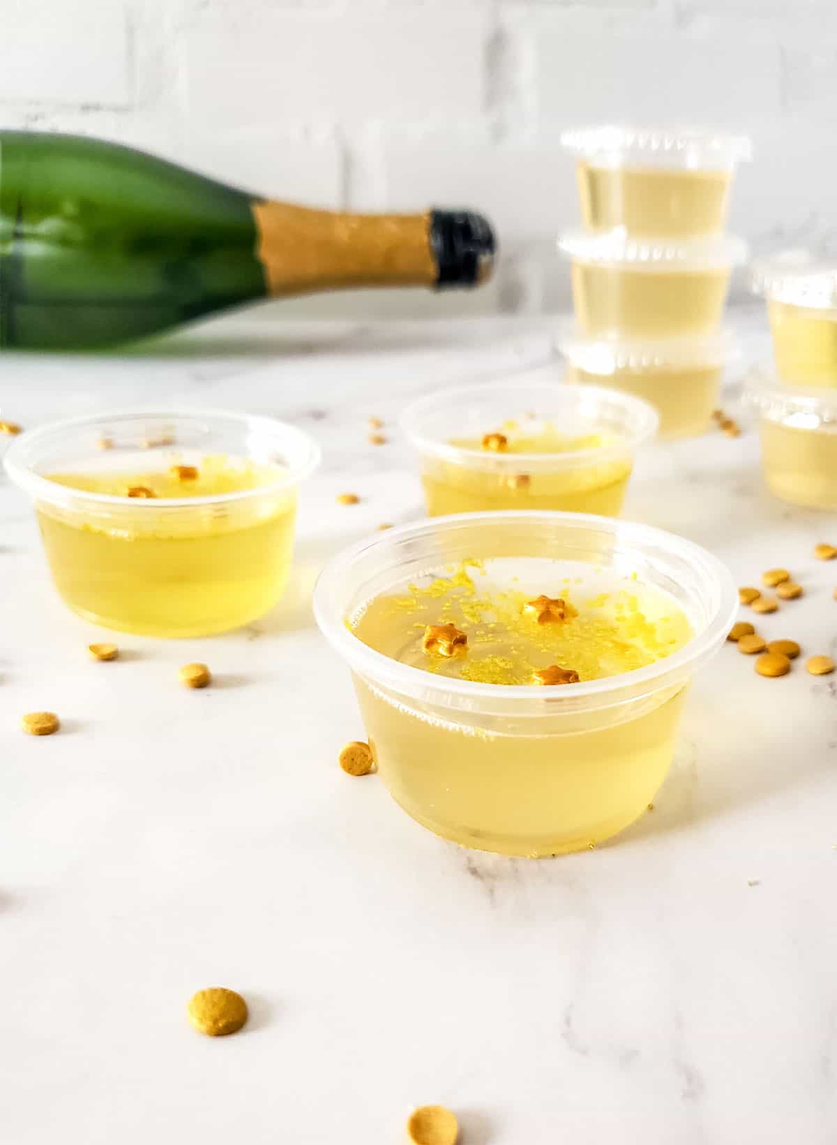 Closeup of champagne jello shots with champagne bottle in back.