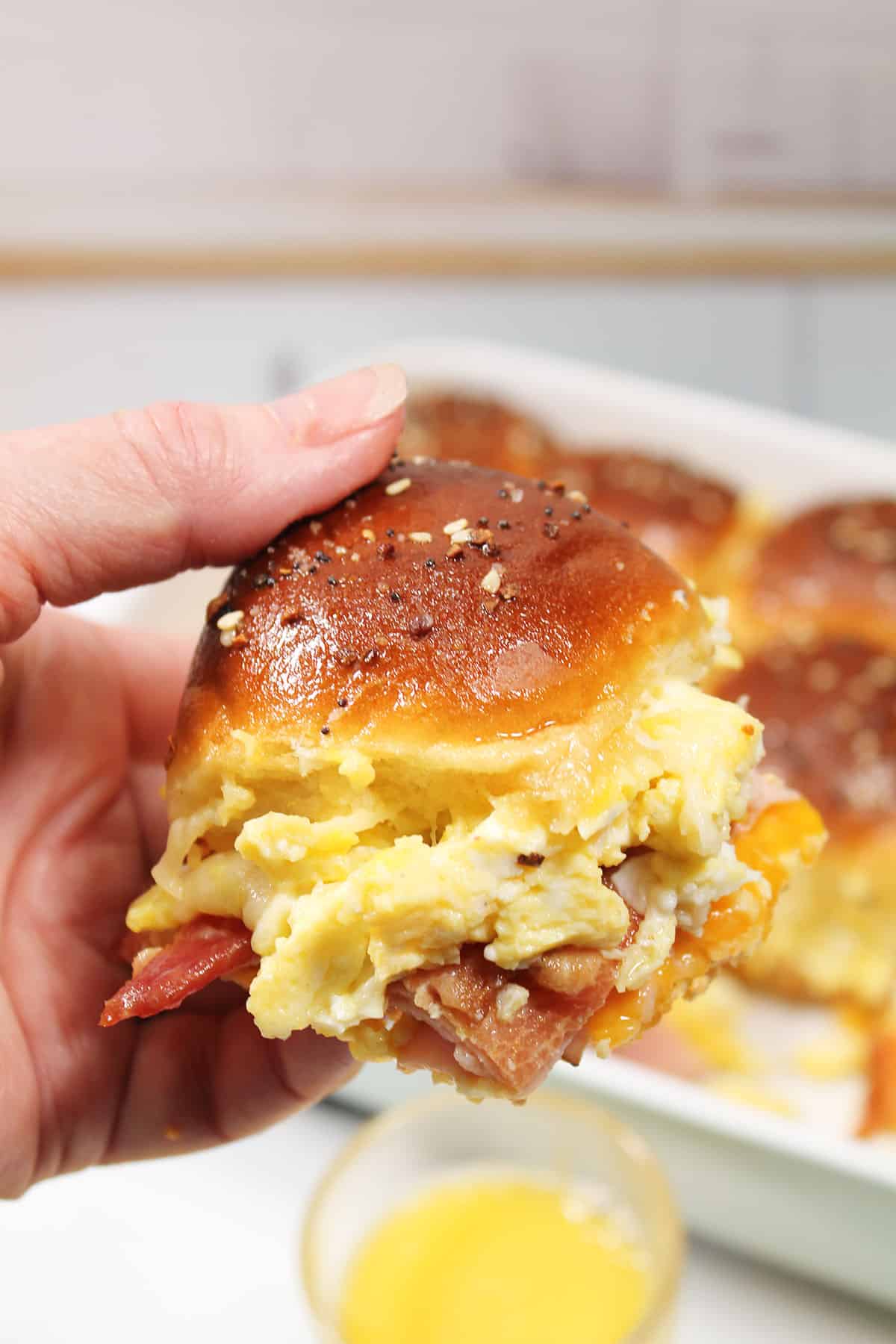 Holding ham and cheese slider over baking dish.
