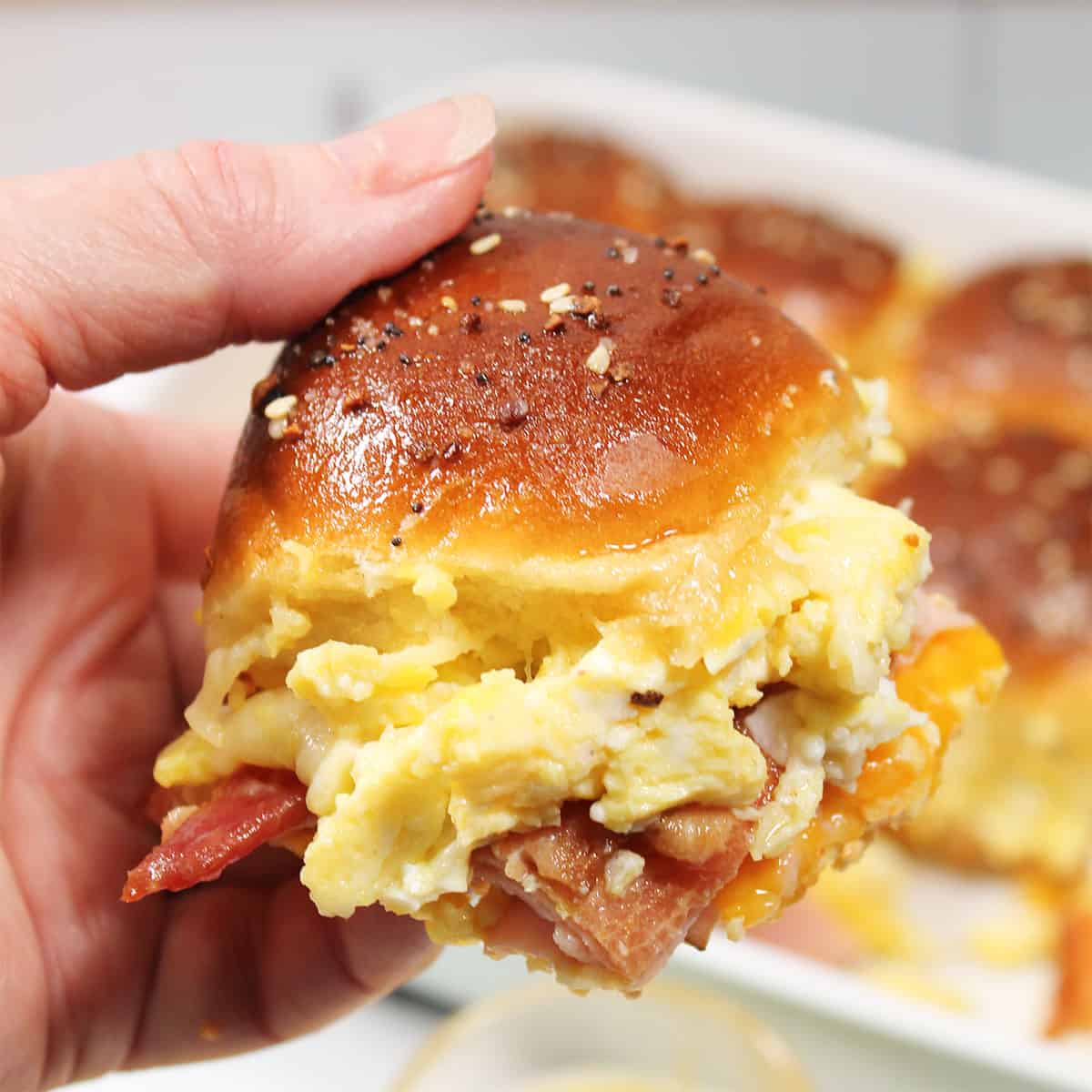 Holding breakfast slider over pan of sliders.