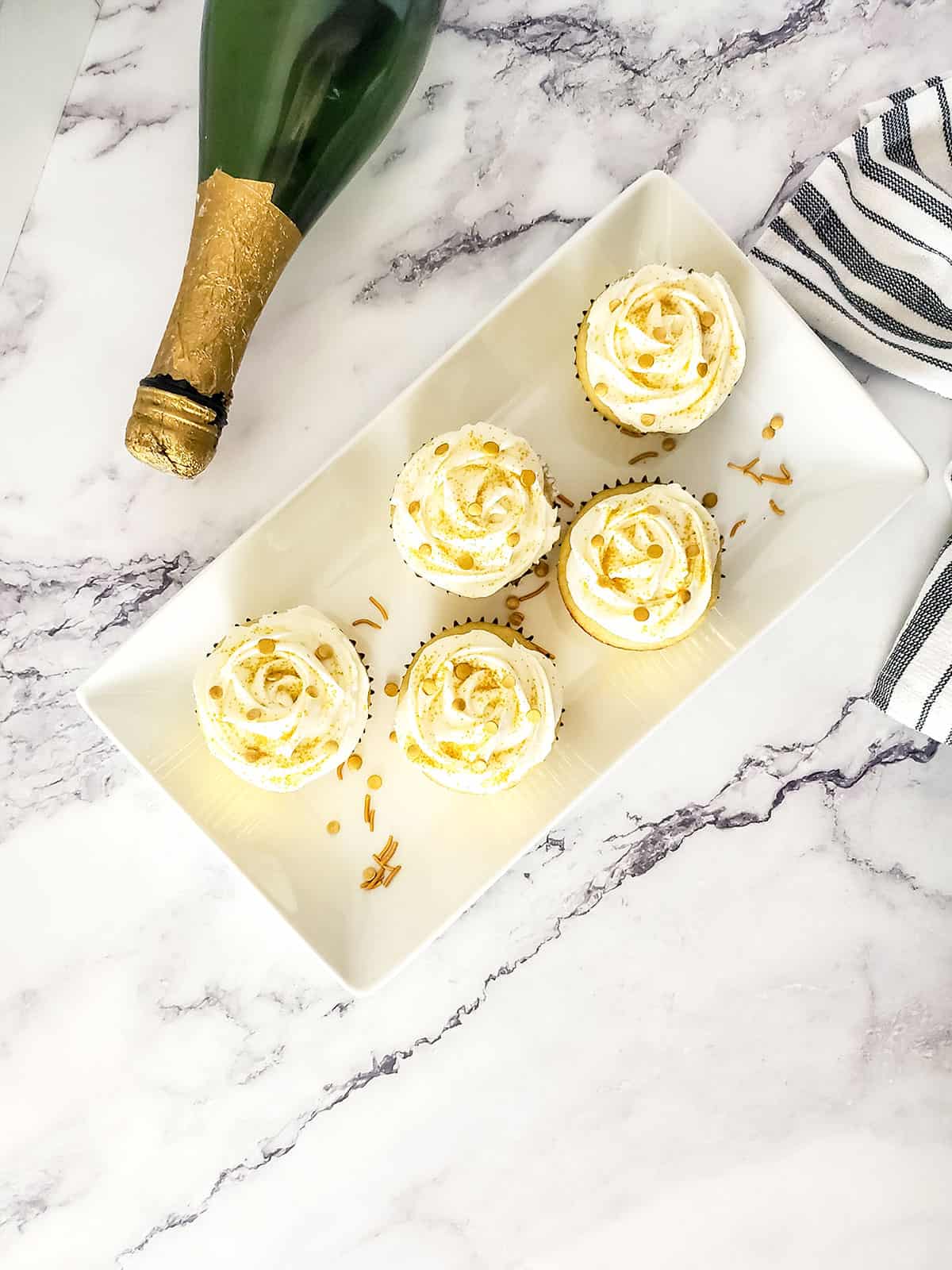 Overhead of cupcakes on platter with champagne bottle.