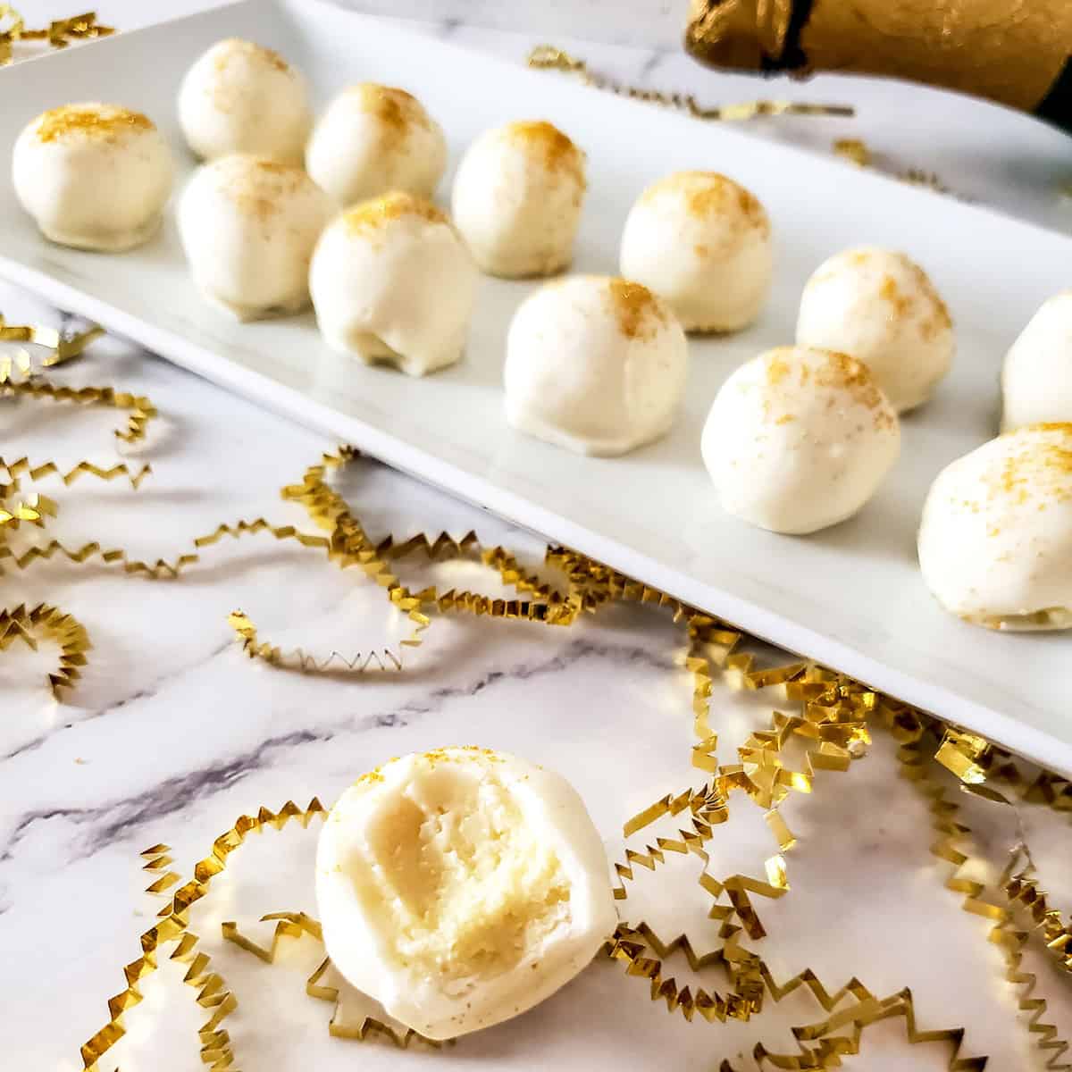 White chocolate champagne truffles on platter with one on table.