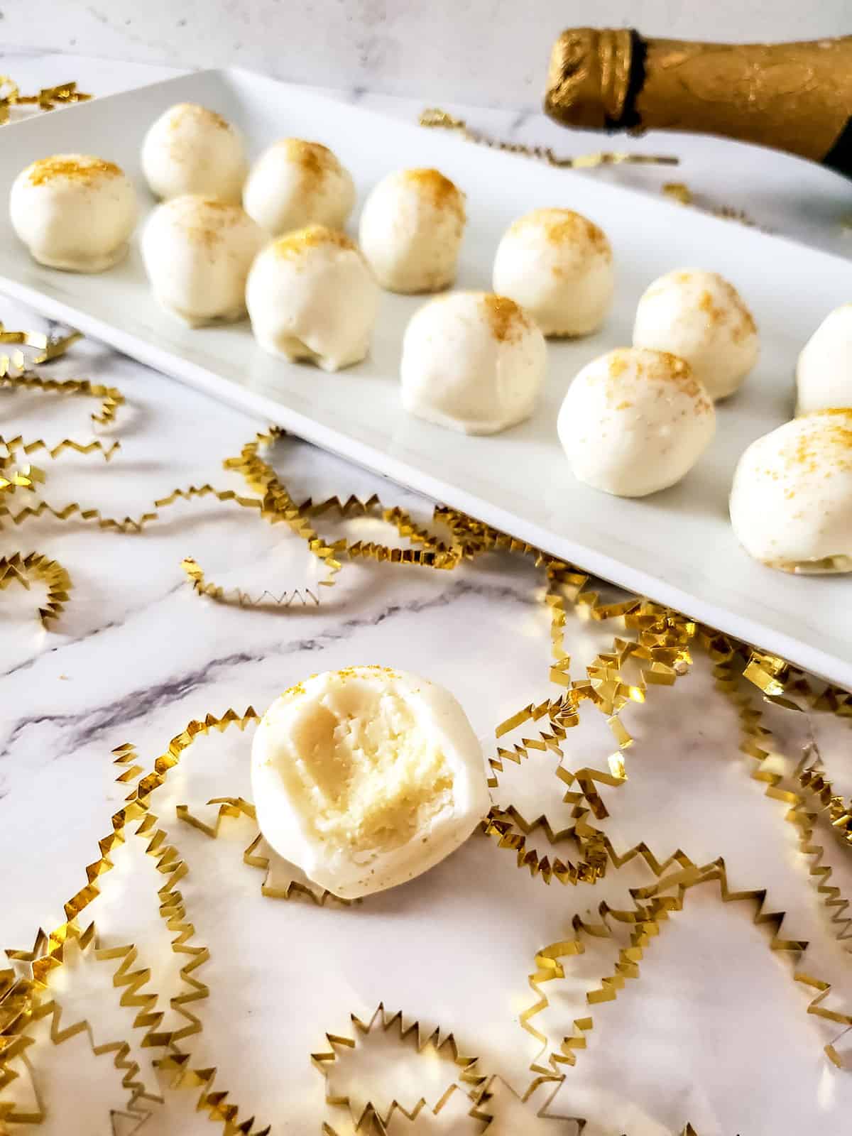 White chocolate champagne truffles with bite out of one on table.