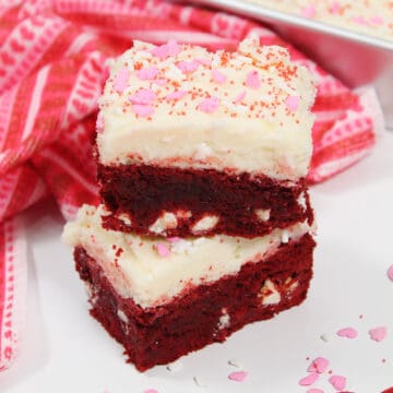Closeup of two red velvet brownies with frosting and sprinkles.
