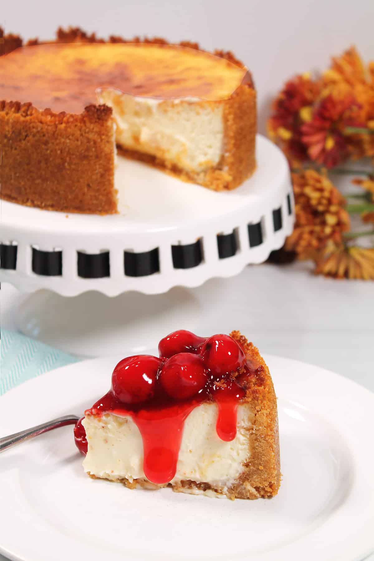 Slice of cheesecake with cherries in front of whole air fryer cheesecake.