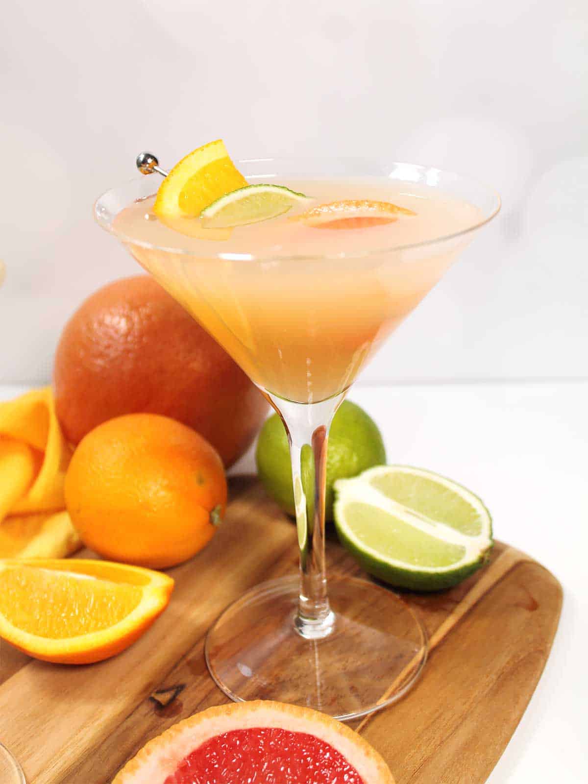 Single grapefruit martini on wooden board with fruit.