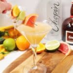 Placing skewer of fruit into grapefruit drink.
