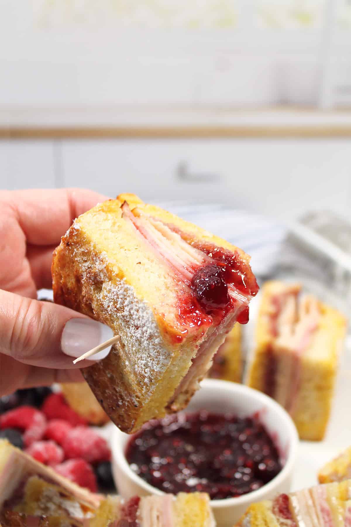 Holding sandwich dipped in raspberry jam.