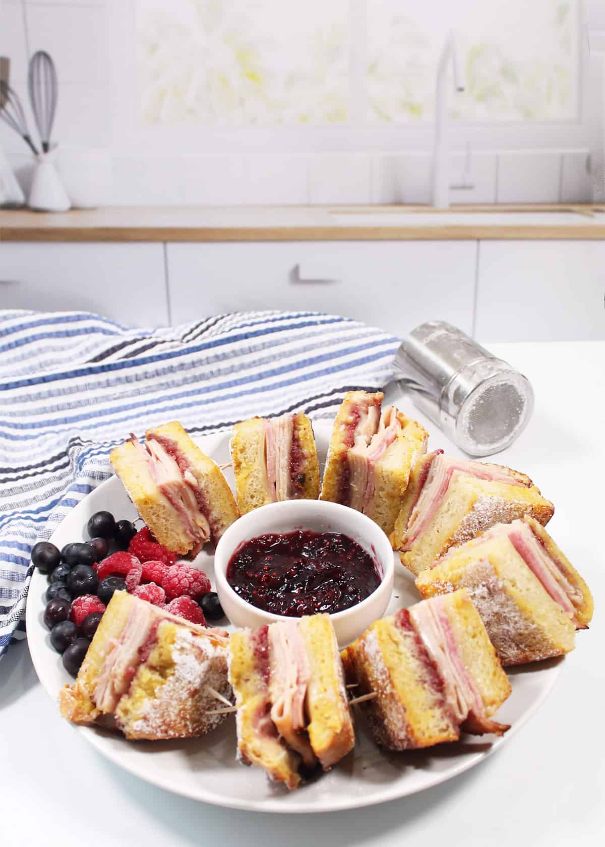 Quartered monte cristo sandwiches on plate with raspberry jam and fruit.