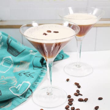 Two espresso martinis on white table by window.