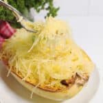 Holding strans of spaghetti squash on fork over squash bowl.