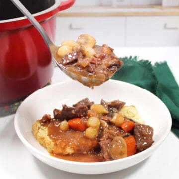 Closeup of ladleful of beef burgundy stew over bowl.