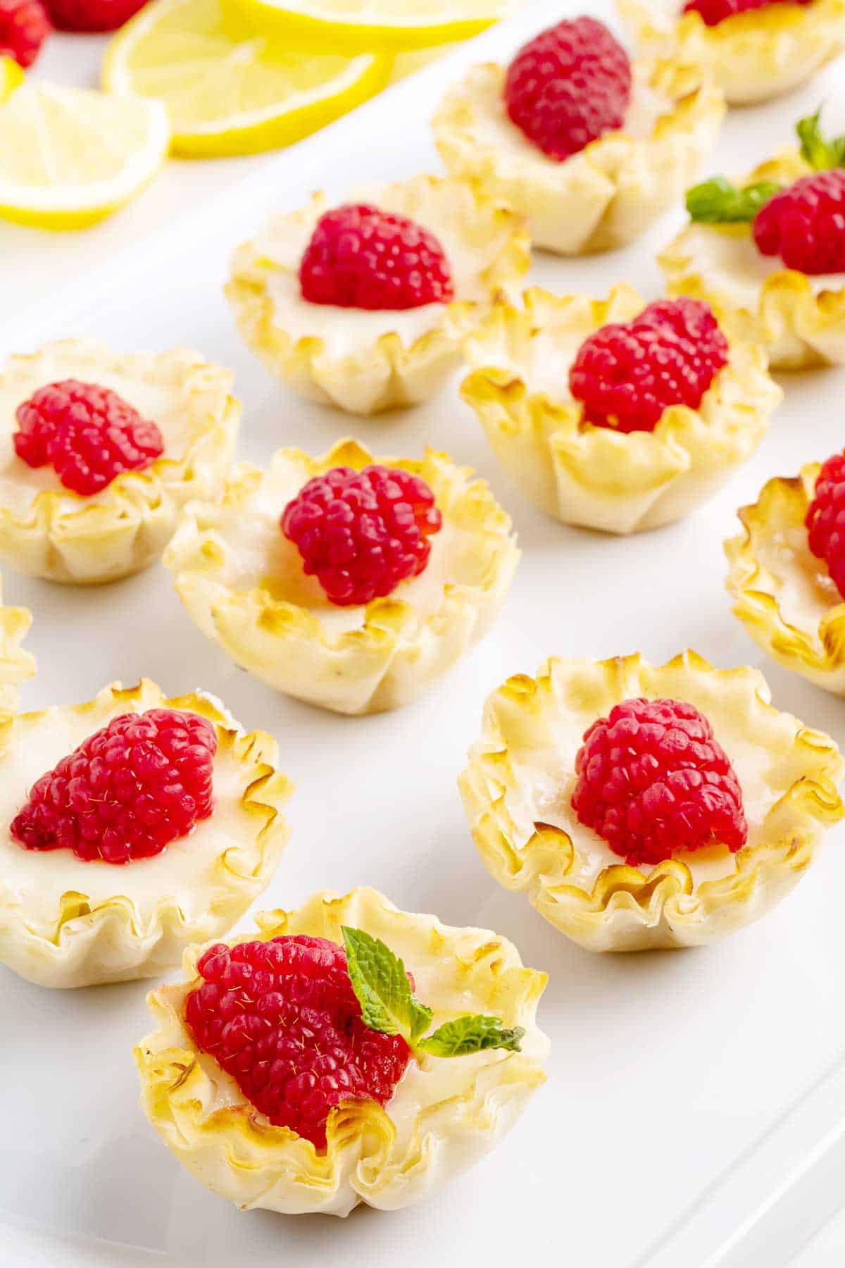 Three rows of mini lemon tarts with raspberry garnish.