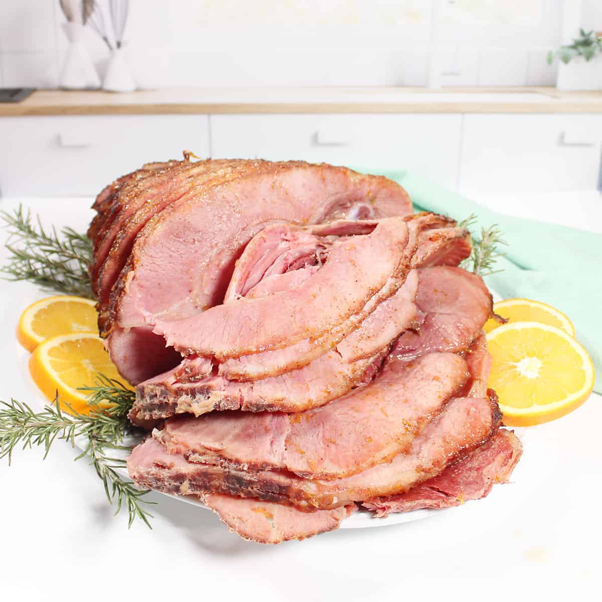 Sliced maple brown sugar glazed ham on platter with orange slices.