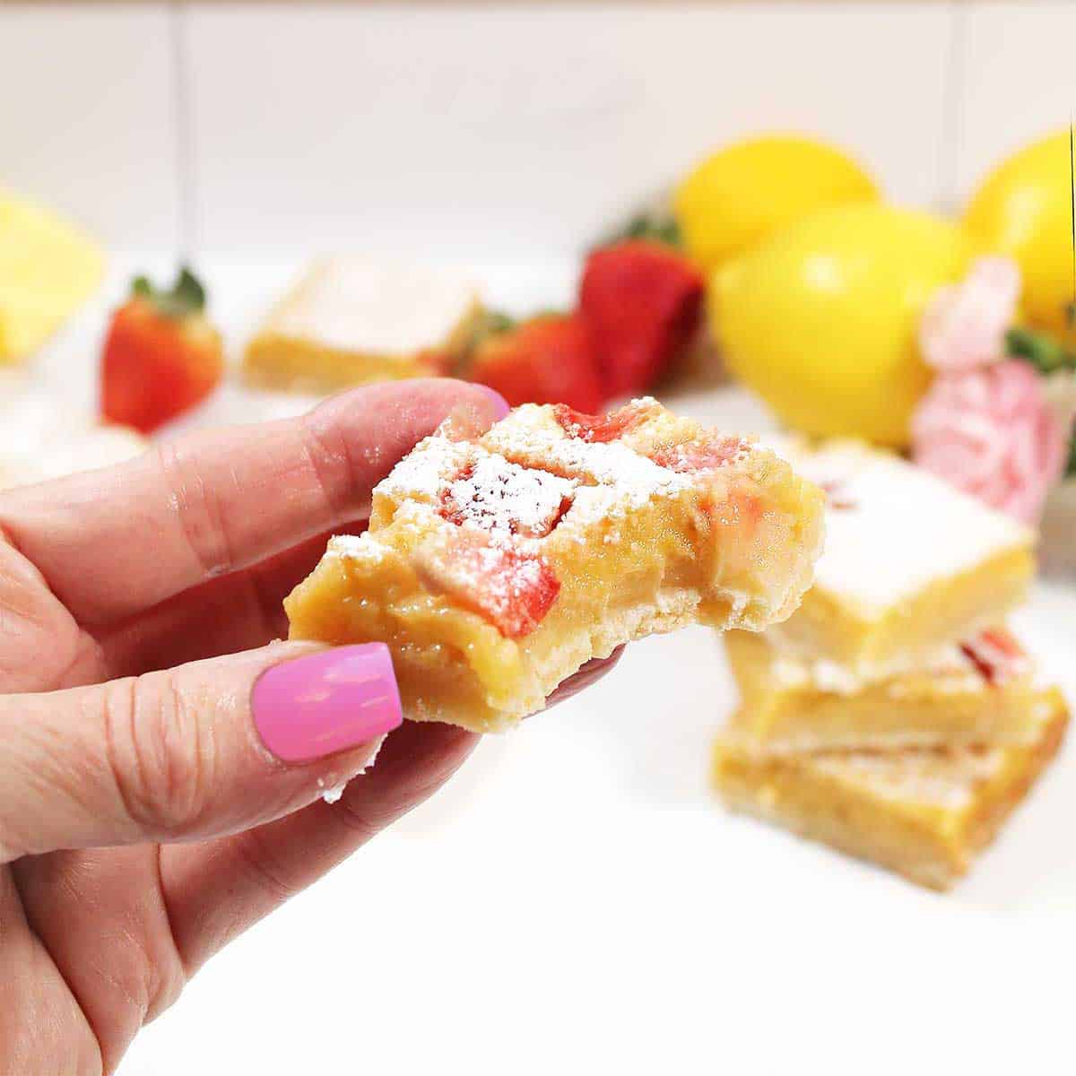 Holding strawberry lemon bar with bite out of it.